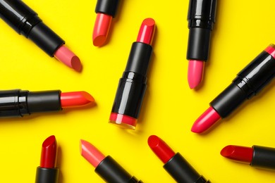 Many bright lipsticks on yellow background, flat lay