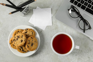 Photo of Chocolate chip cookies, tea and laptop on light gray table at workplace, flat lay