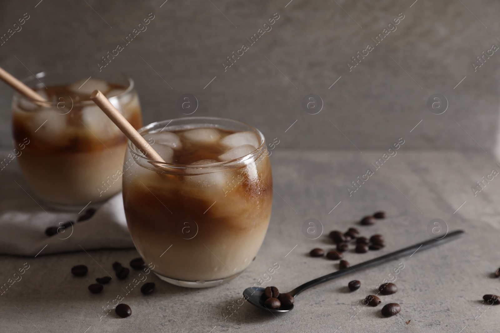 Photo of Refreshing iced coffee with milk in glasses, beans and spoon on gray table, closeup. Space for text