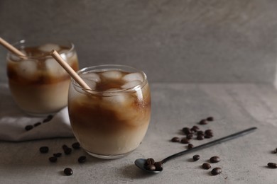 Photo of Refreshing iced coffee with milk in glasses, beans and spoon on gray table, closeup. Space for text