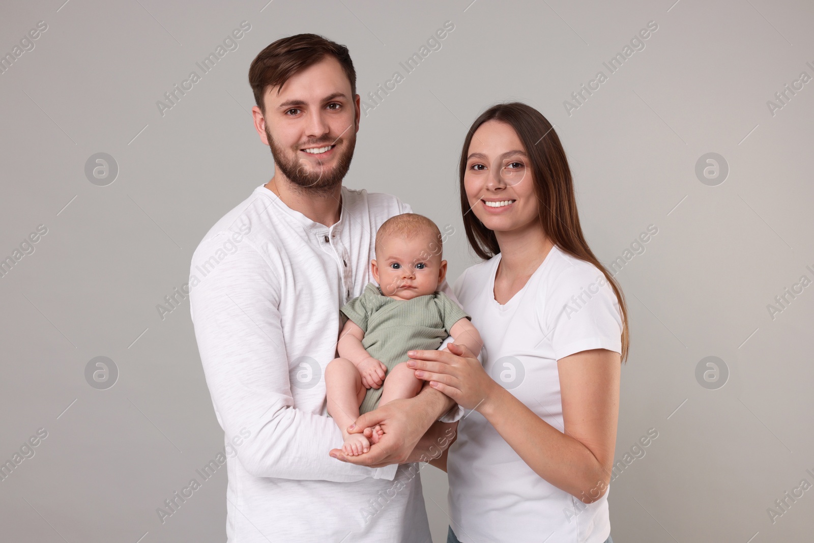 Photo of Happy family. Parents with their cute baby on grey background