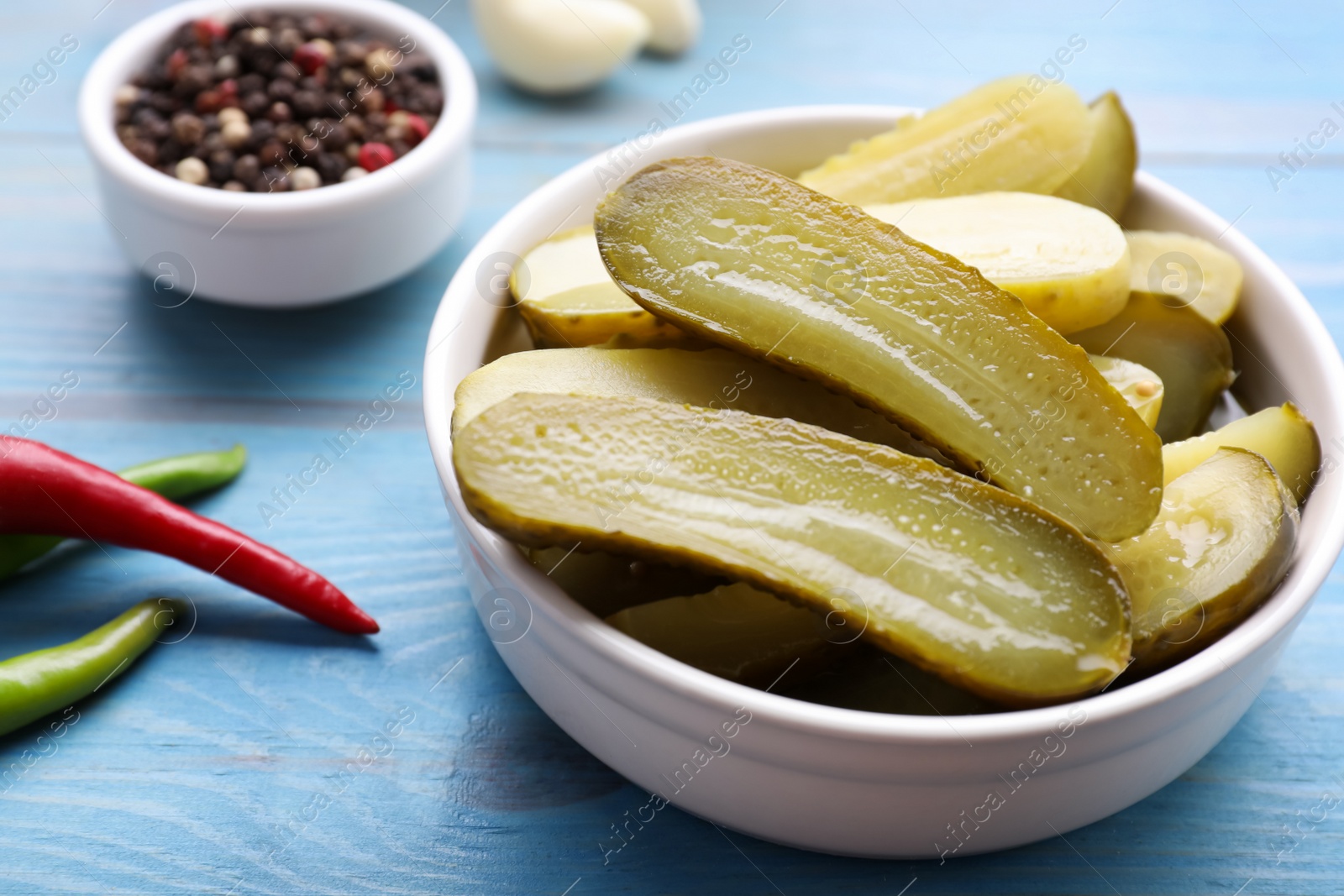 Photo of Pickled cucumbers and spices on light blue wooden table, closeup