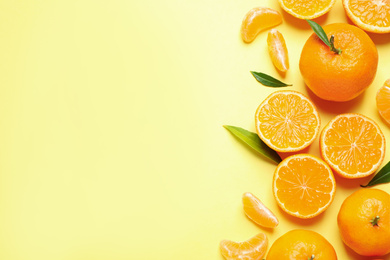 Flat lay composition with fresh ripe tangerines and leaves on light yellow background, space for text. Citrus fruit