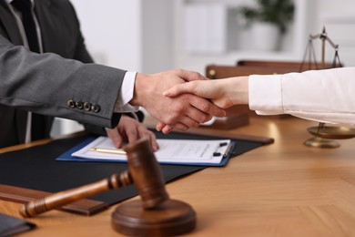 Notary shaking hands with client at wooden table in office, closeup