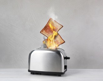 Image of Toaster flaming up while cooking slices of bread on white wooden table. Unsafe appliance 