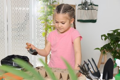 Photo of Little girl adding soil into peat pots at table in room. Growing vegetable seeds