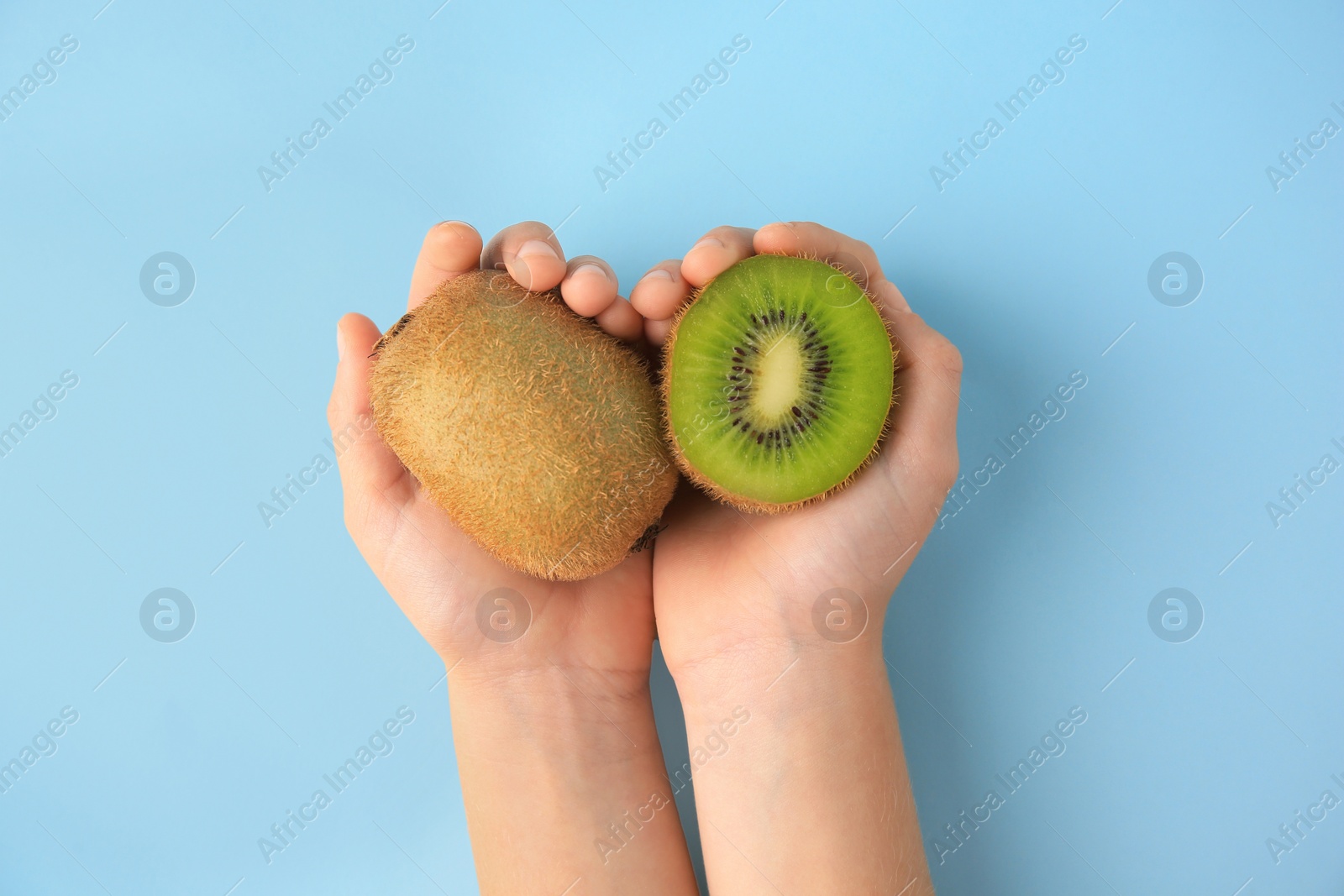 Photo of Woman holding cut and whole fresh kiwis on light blue background, top view