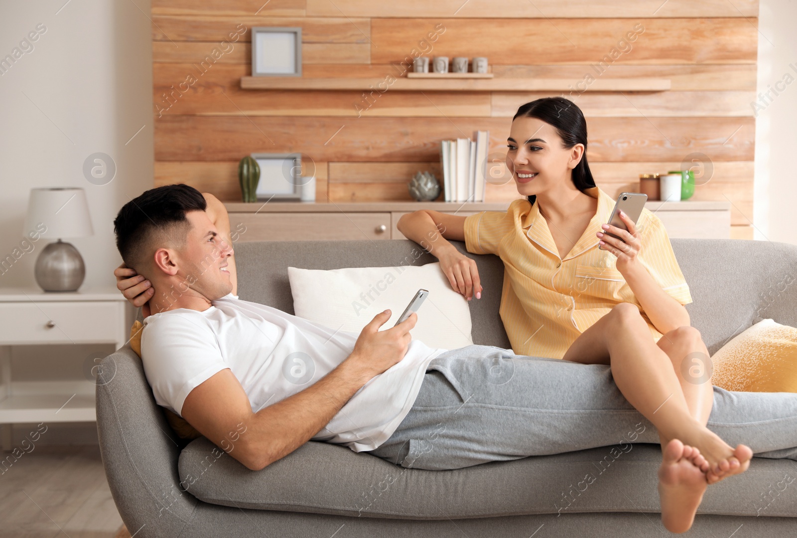 Photo of Happy couple in pyjamas with gadgets spending time together on sofa at home