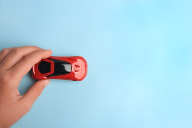 Child playing with toy car on light blue background, top view. Space for text
