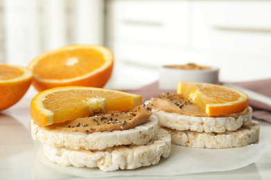 Photo of Puffed rice cakes with peanut butter and orange on white table, closeup