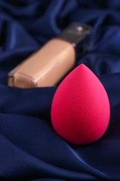 Photo of Pink makeup sponge on blue silk cloth, closeup