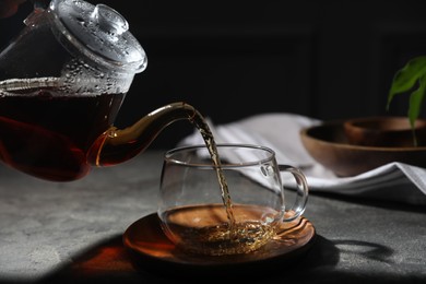 Photo of Pouring hot tea into cup on grey table, closeup