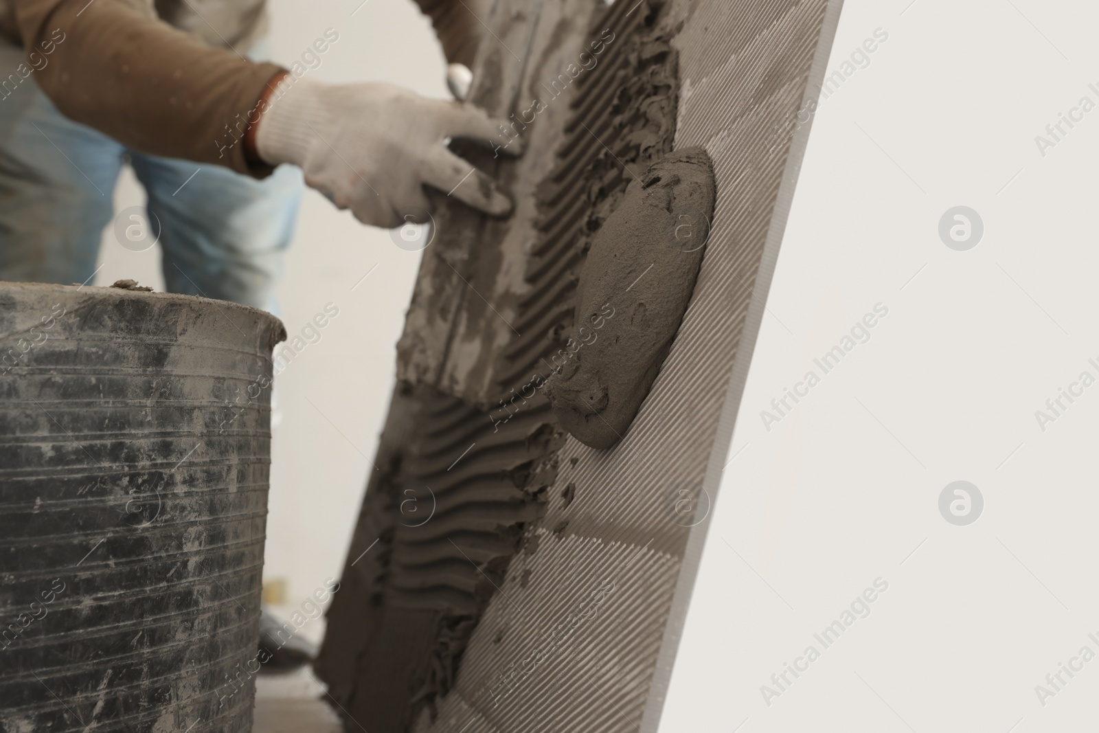 Photo of Worker applying cement on wall tile for installation indoors, closeup