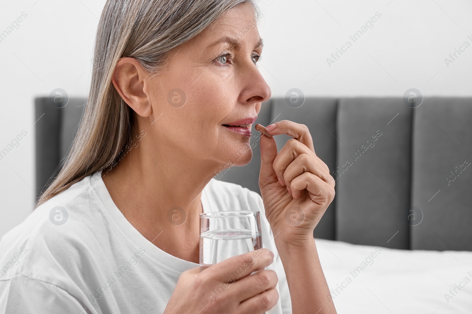 Photo of Beautiful woman taking vitamin pill in bedroom