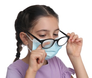 Little girl wiping foggy glasses caused by wearing medical face mask on white background. Protective measure during coronavirus pandemic