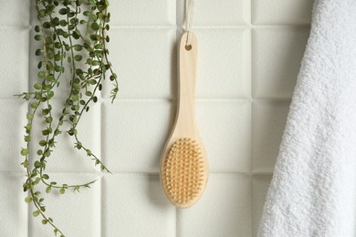 Photo of Bath accessories. Bamboo brush, terry towel and green plant on white tiled wall