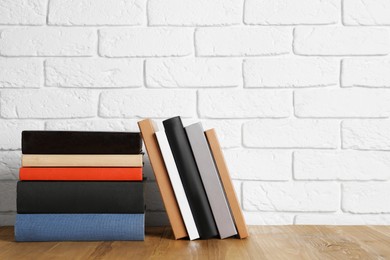 Photo of Books on wooden table near white brick wall, space for text