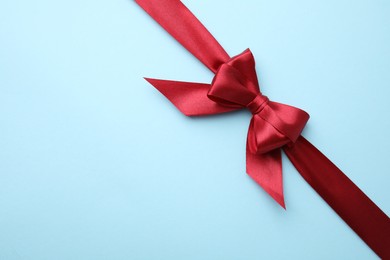 Photo of Red satin ribbon with bow on light blue background, top view