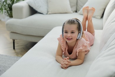 Photo of Little girl with headphones lying on comfortable sofa in living room