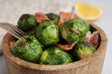 Photo of Delicious roasted Brussels sprouts and bacon in bowl on table, closeup