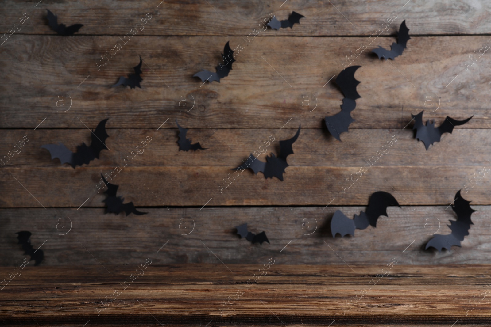 Photo of Empty wooden table near wall decorated with paper bats. Halloween celebration