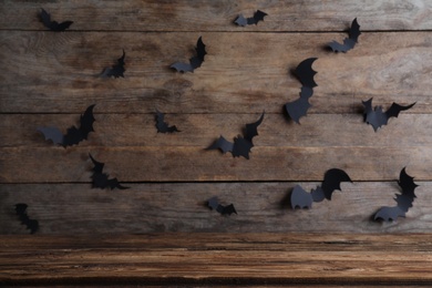 Photo of Empty wooden table near wall decorated with paper bats. Halloween celebration