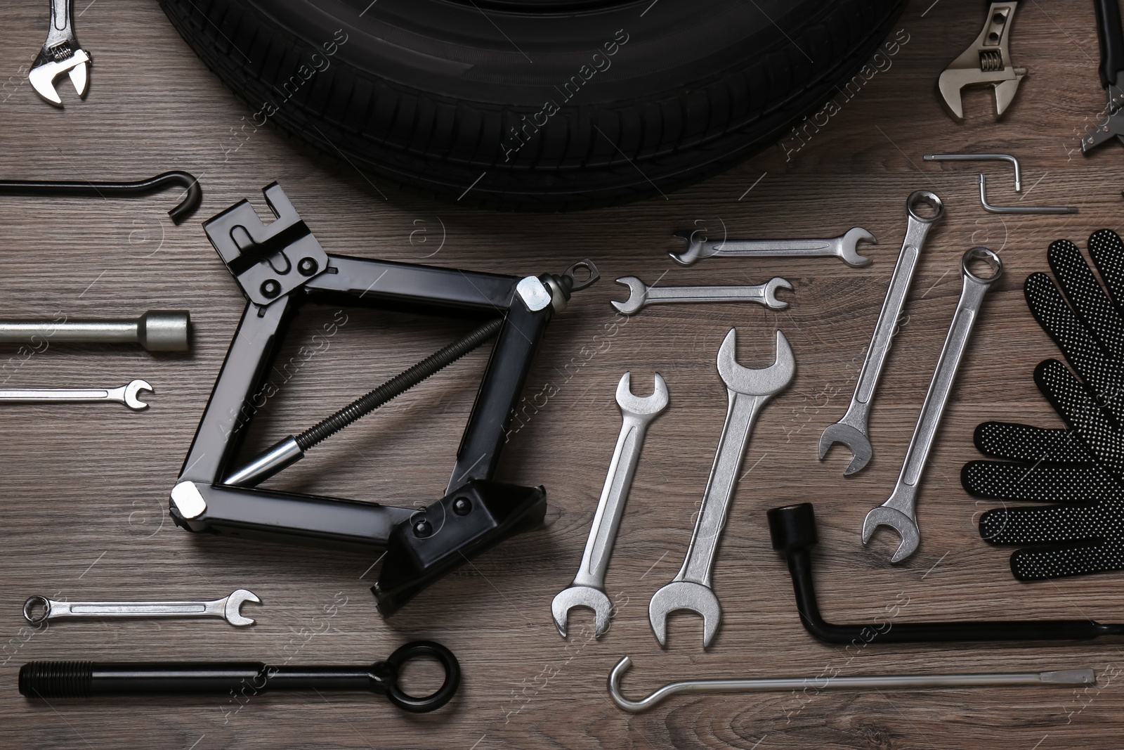 Photo of Car wheel, scissor jack, gloves and different tools on wooden surface, flat lay