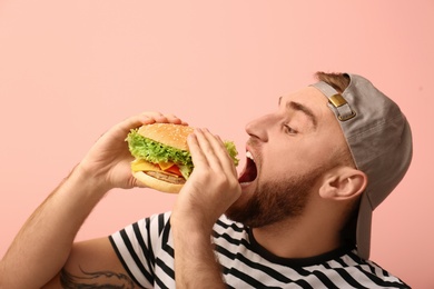 Photo of Young man eating tasty burger on color background