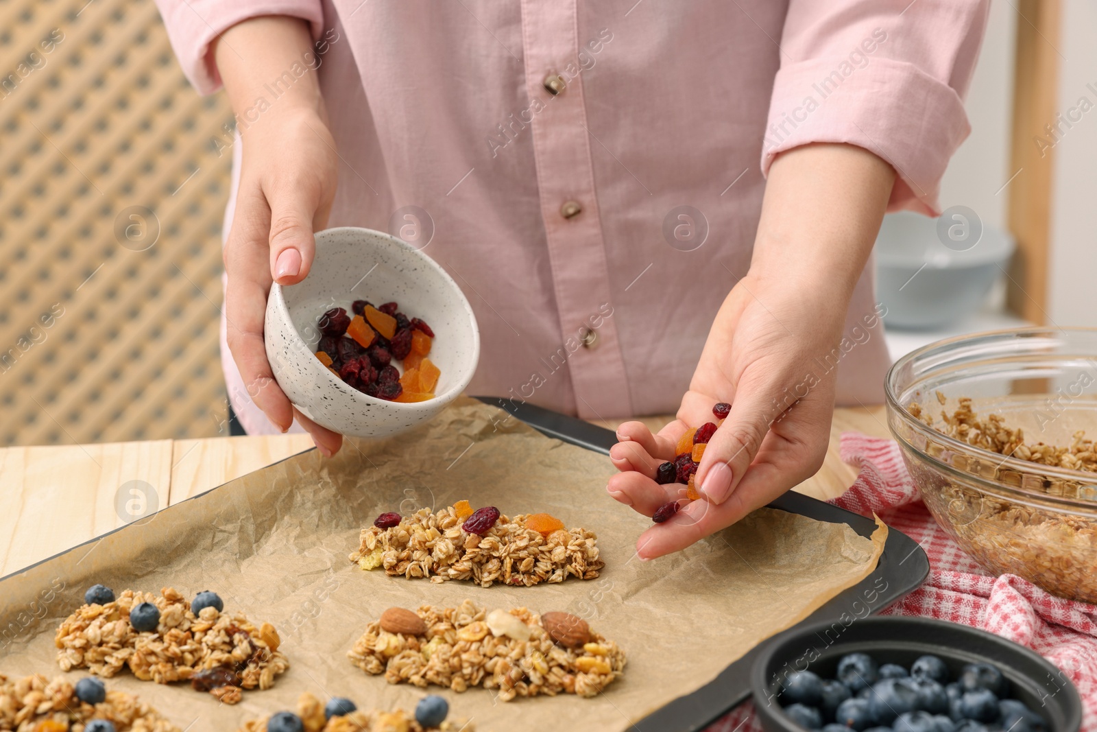 Photo of Making granola bars. Woman with dry fruits at table in kitchen, closeup