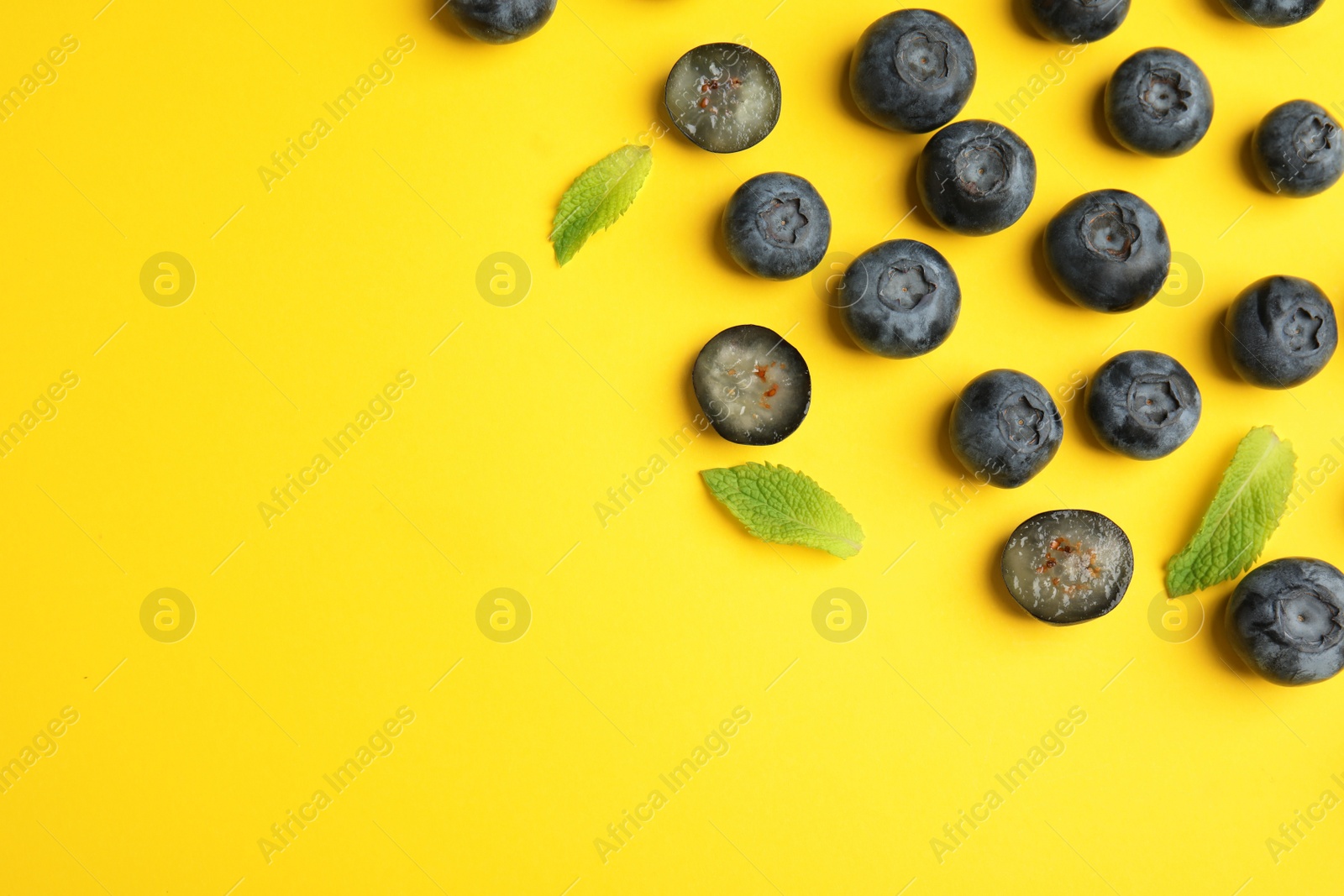 Photo of Tasty ripe blueberries and leaves on yellow background, flat lay with space for text