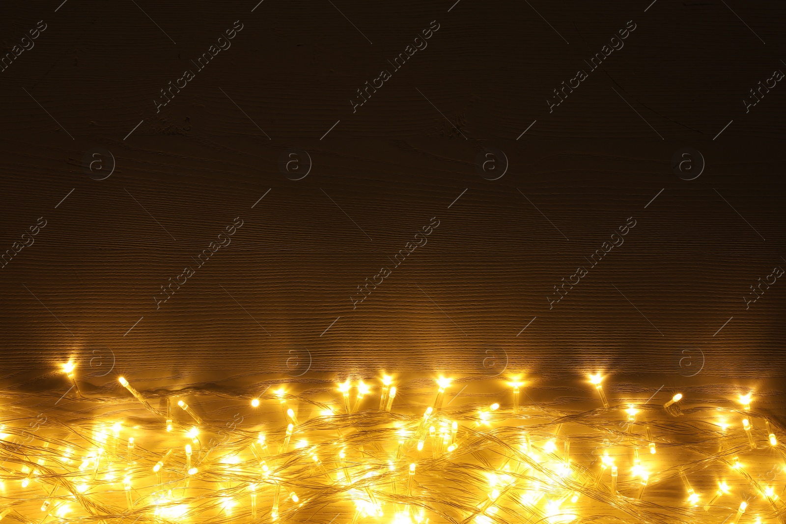 Photo of Beautiful glowing Christmas lights on wooden table, top view. Space for text