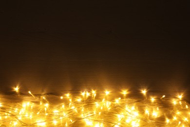 Photo of Beautiful glowing Christmas lights on wooden table, top view. Space for text