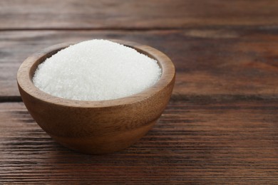 Photo of Granulated sugar in bowl on wooden table, closeup. Space for text