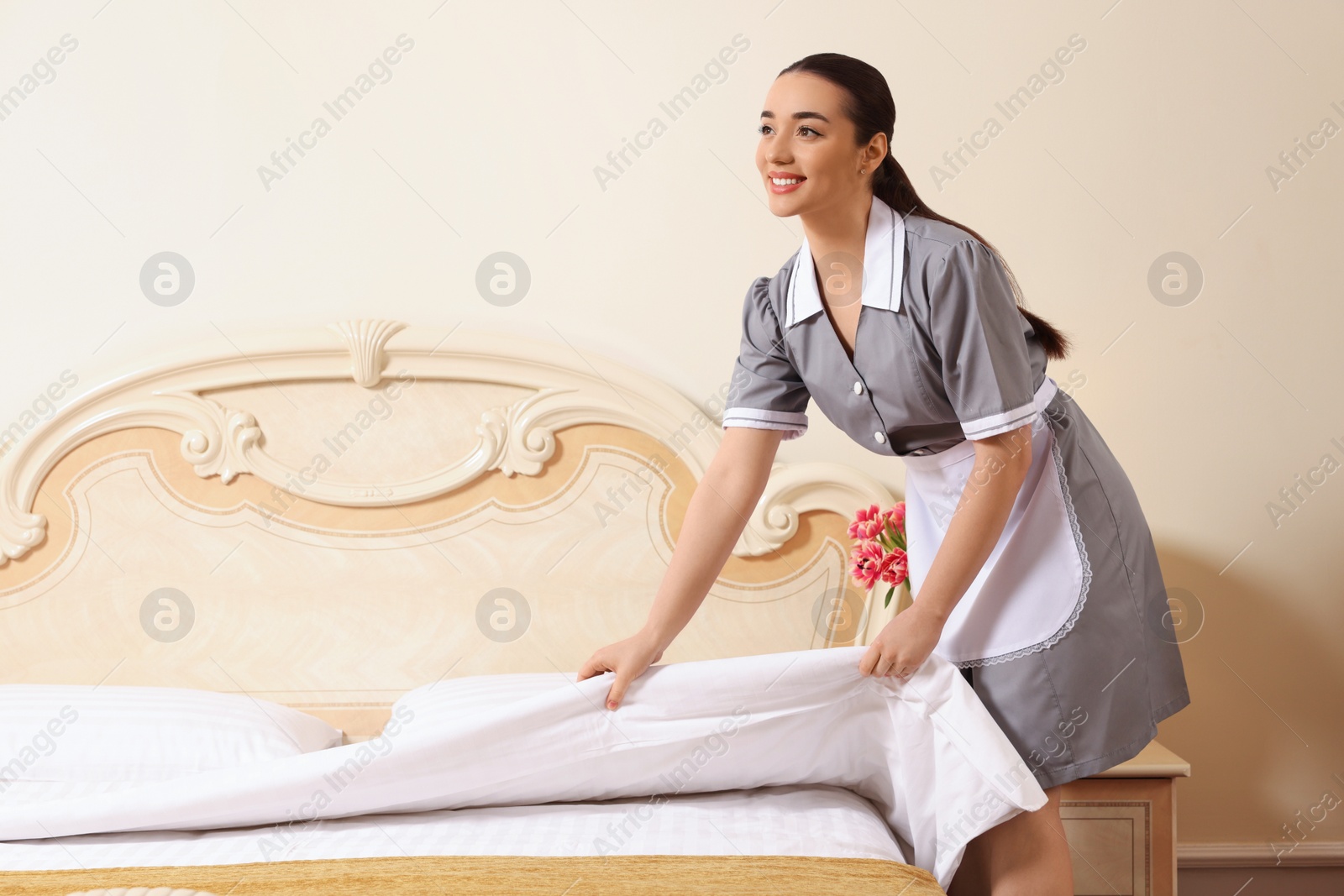 Photo of Young chambermaid making bed in hotel room. Space for text