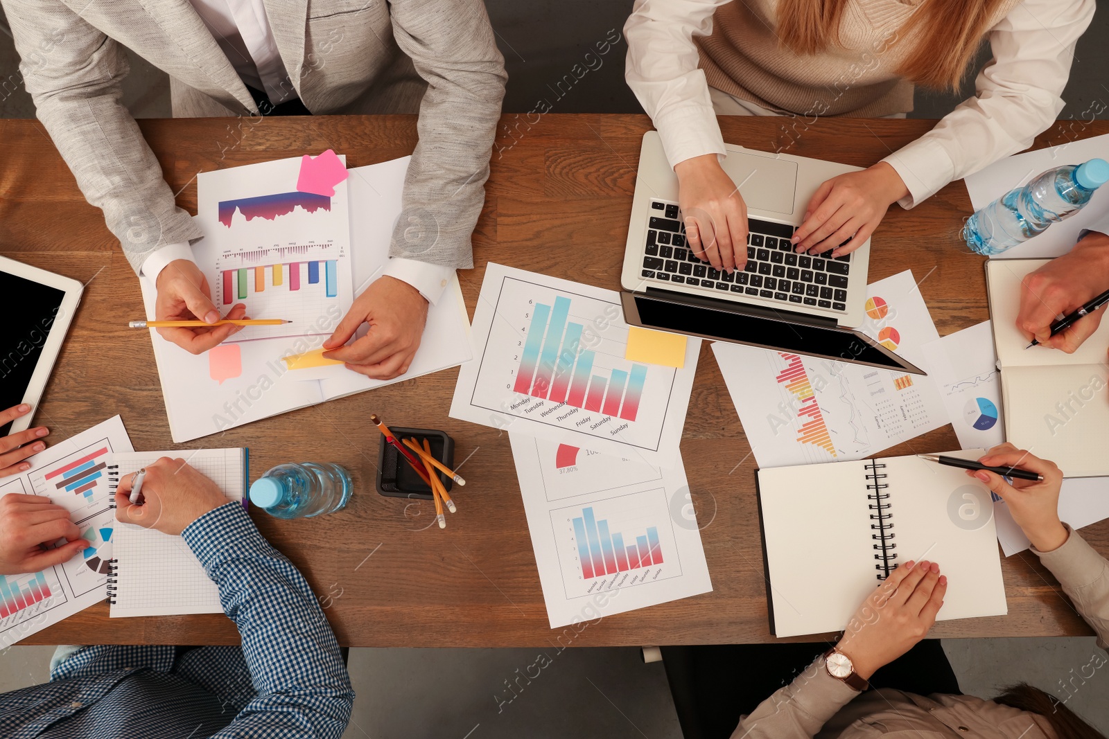 Photo of Team of employees working together at wooden table in office, above view