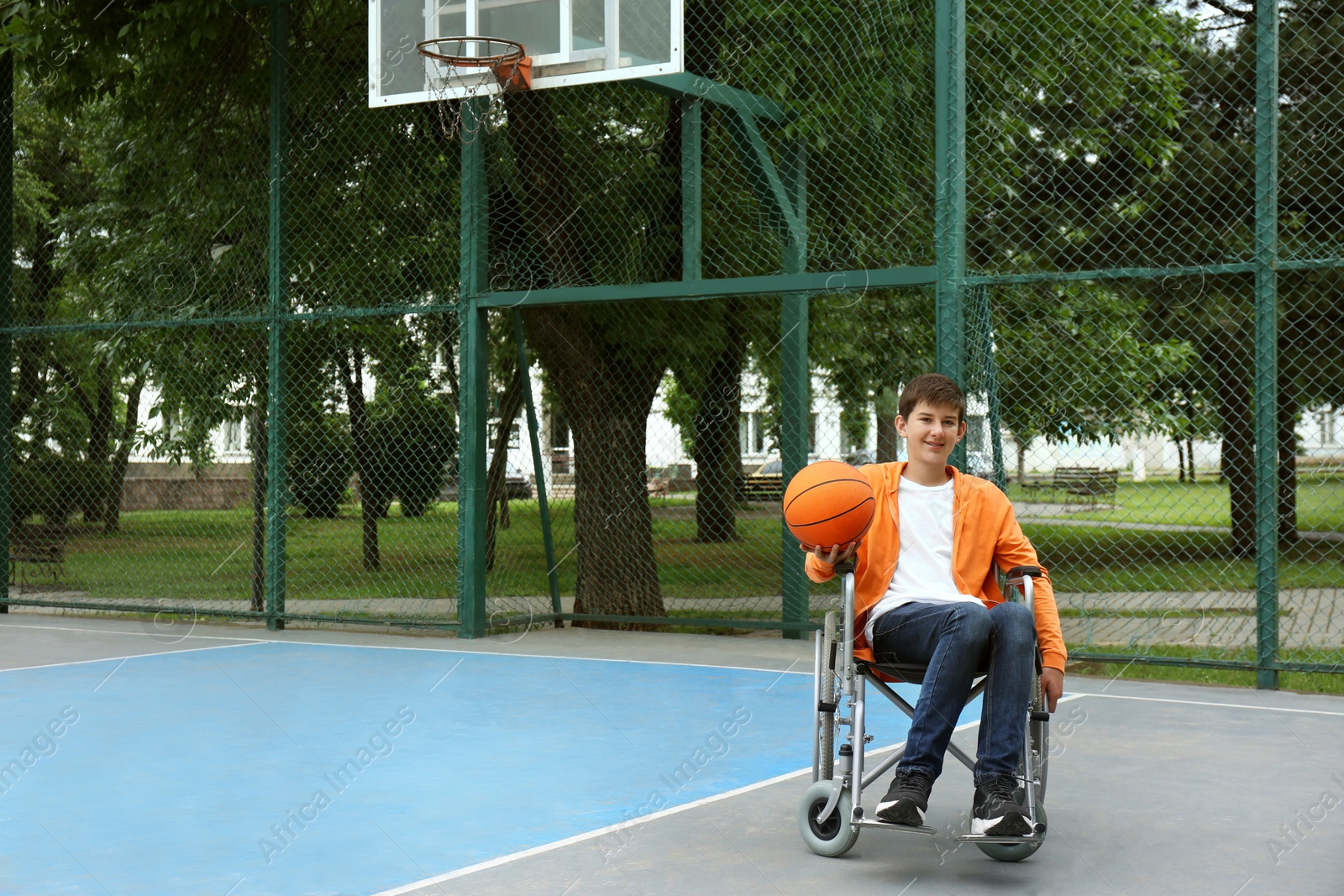 Photo of Disabled teenage boy in wheelchair with basketball ball at outdoor court