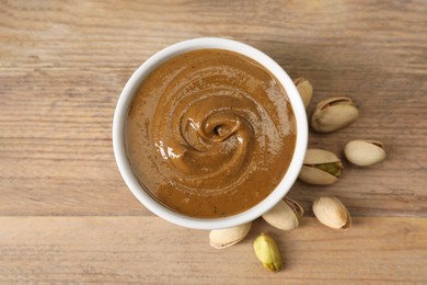 Photo of Delicious nut butter in bowl and pistachios on wooden table, top view