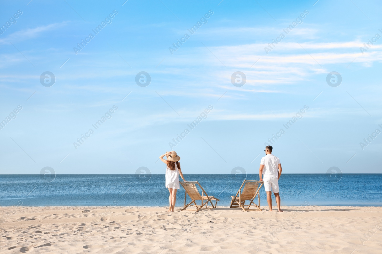 Photo of Young couple near deck chairs on sandy beach