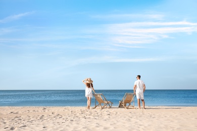 Photo of Young couple near deck chairs on sandy beach