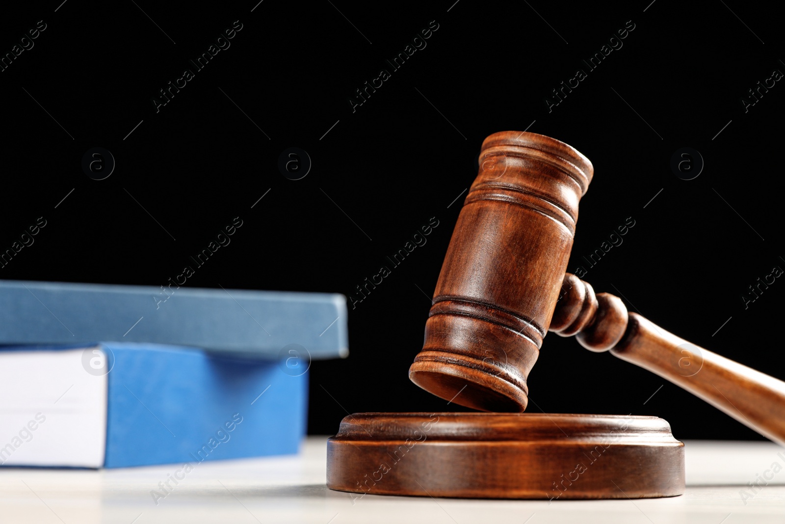 Photo of Judge's gavel and books on white table against black background. Criminal law concept