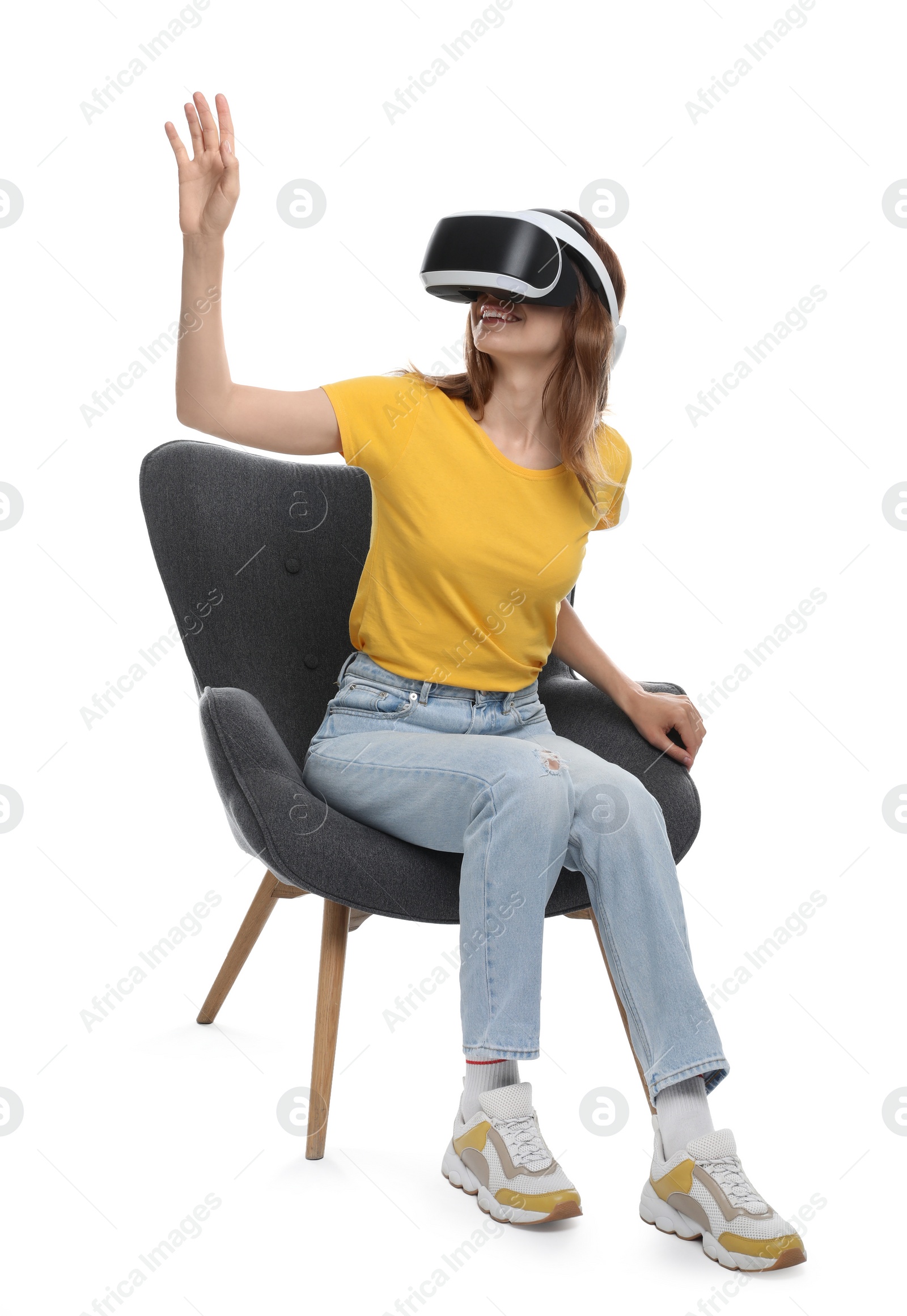 Photo of Smiling woman using virtual reality headset while sitting in armchair against white background