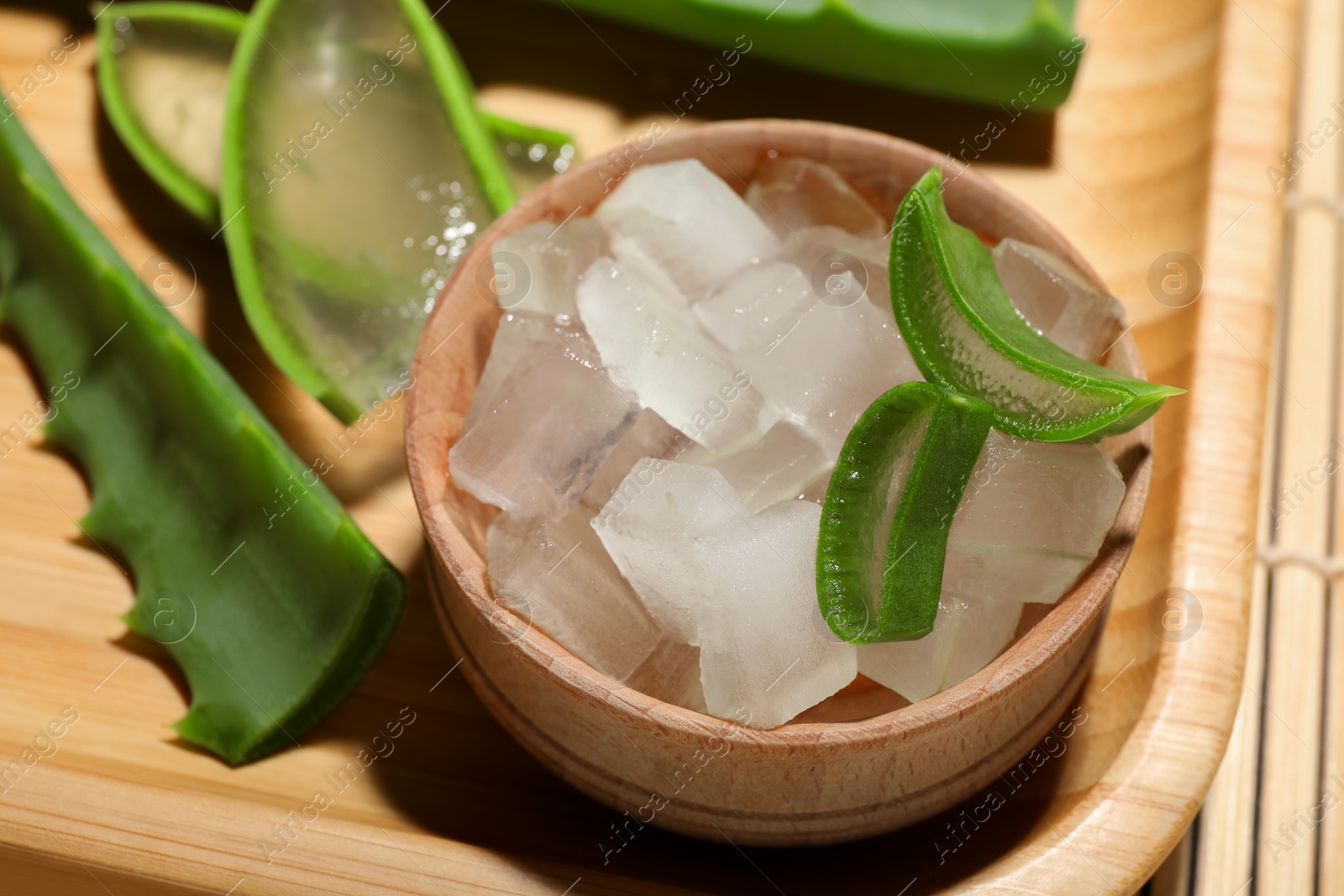 Photo of Aloe vera gel and slices of plant on bamboo mat, closeup