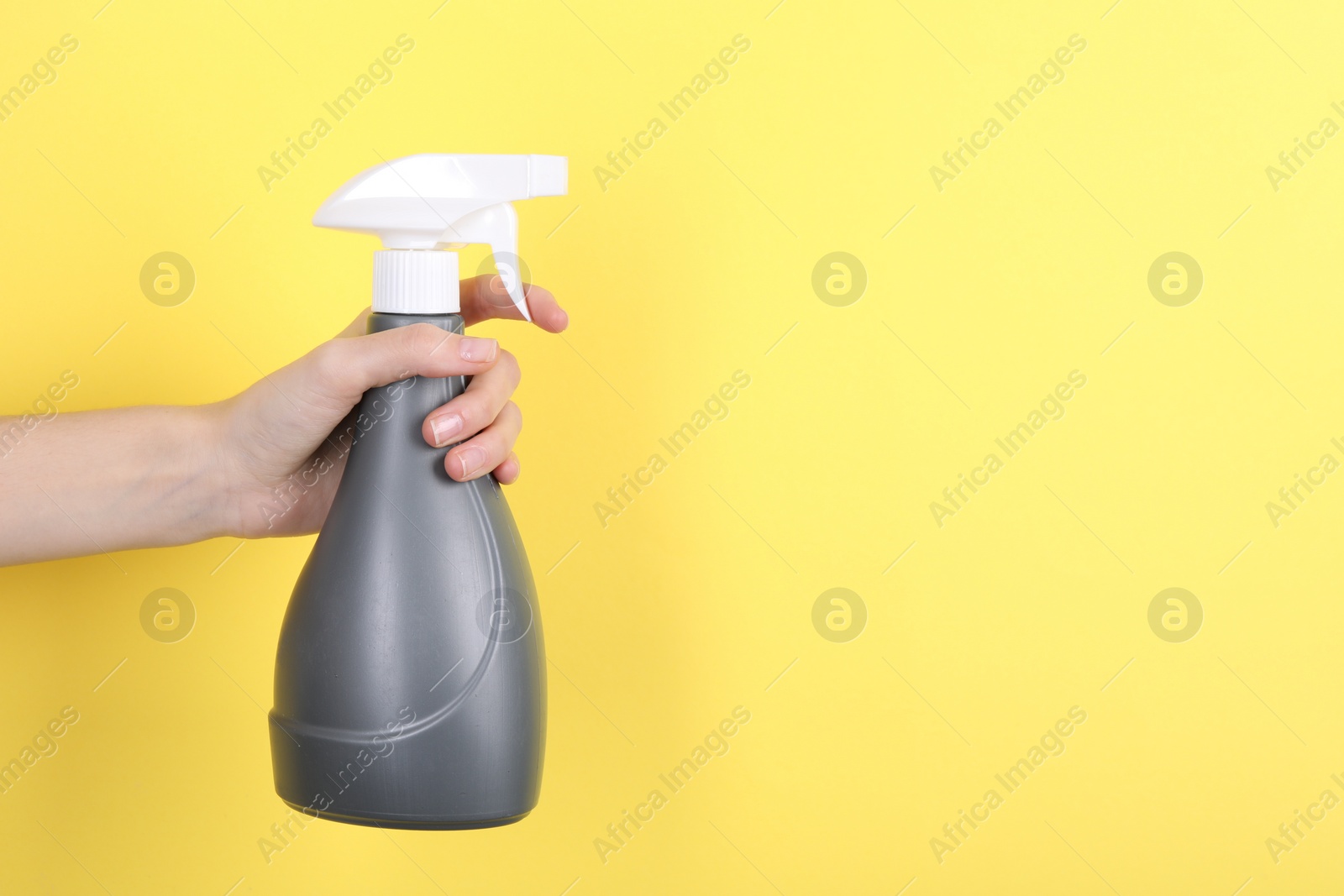 Photo of Woman holding plastic spray bottle on yellow background, closeup. Space for text