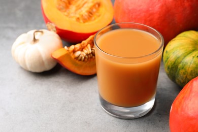 Photo of Tasty pumpkin juice in glass and different pumpkins on light grey table. Space for text
