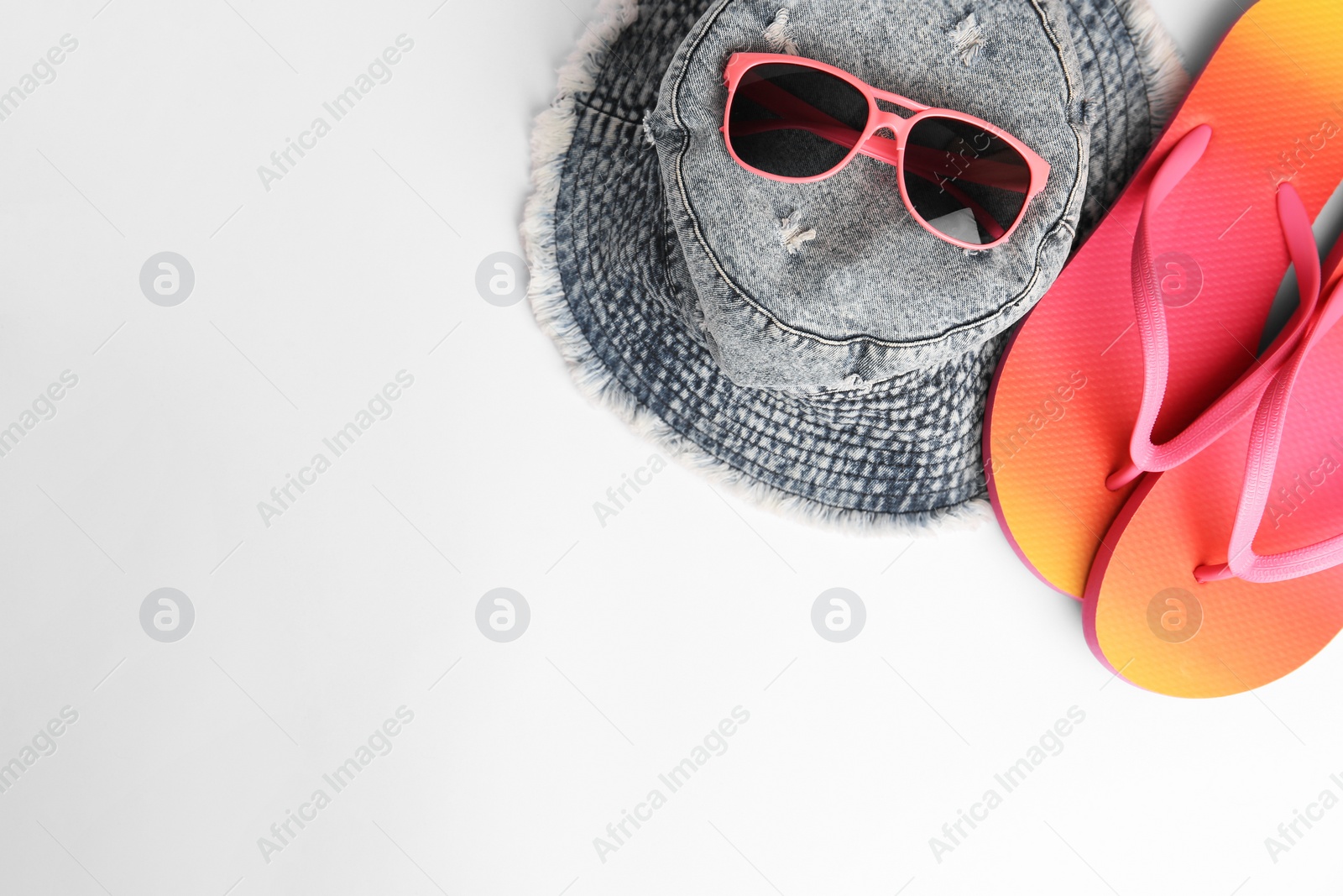 Photo of Sunglasses, hat and bright flip flops on white background, flat lay with space for text. Beach accessories