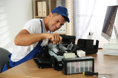 Photo of Repairman with screwdriver fixing modern printer in office