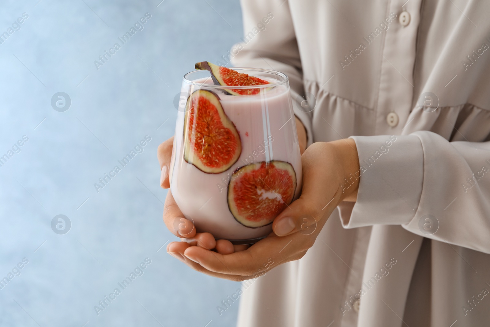 Photo of Woman holding fig smoothie on light blue background, closeup