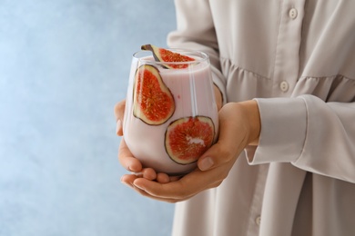 Photo of Woman holding fig smoothie on light blue background, closeup