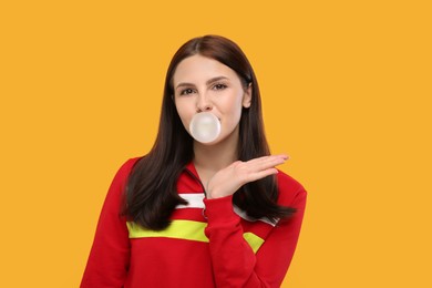 Photo of Beautiful woman blowing bubble gum on orange background