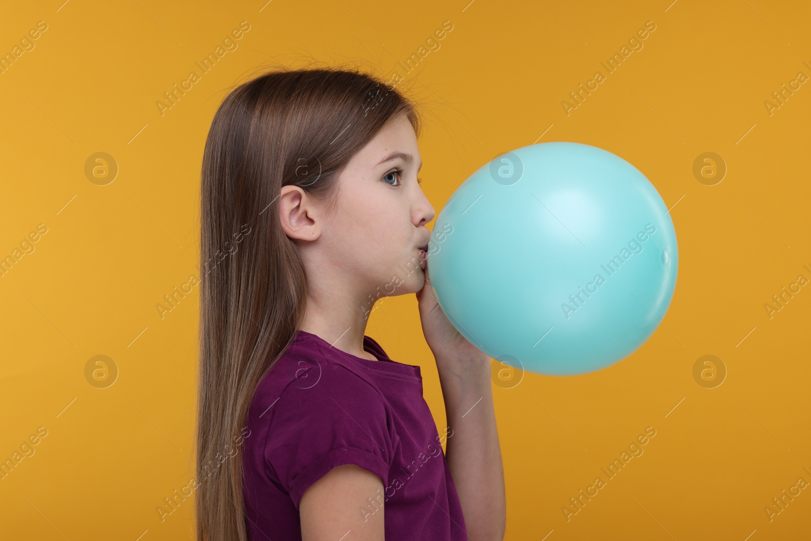 Photo of Girl inflating bright balloon on orange background